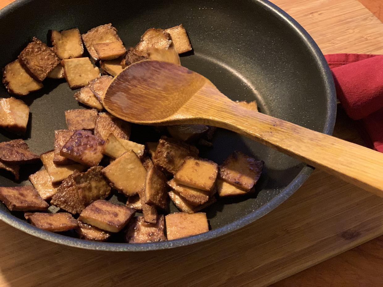 Knusprige braune Räuchertofu-Plättchen in einer Pfanne mit Holzkochlöffel